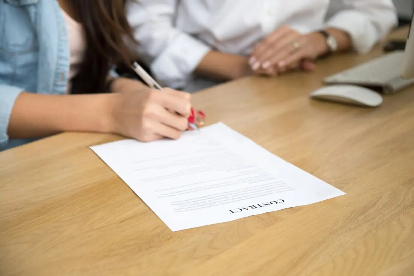 A woman signing a contract, with a female hand placing a written signature on the document.